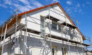 Gerüst um Haus für Fassaden Sanierung. Weiße Wände, rote Ziegel und blauer Himmel.