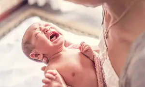 Bebé llorando con espasmos infantiles, envuelto en una manta rosa, sostenido por una persona.