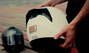 Ręce trzymają biały kask motocyklowy. Obok leży czarny kask. Dylemat: kask szczękowy czy integralny?