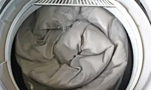 A grey comforter is being washed in a washing machine, showing the best way to wash a comforter. Water is splashing onto the fabric.