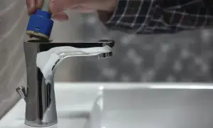 Dłoń wkłada niebieski wkład do chromowanego kranu.