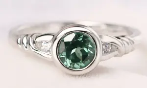 Anillo de plata con piedra verde ovalada y dos pequeños diamantes a cada lado, sujeto con un engaste bisel.