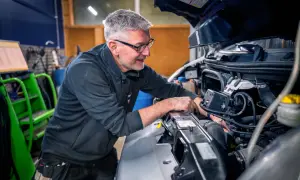 Mekaniker med glasögon arbetar med att serva bilens motor.