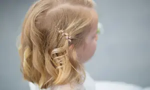 Urocze fryzury ze spinką z boku, ozdobioną listkami, dodają blasku blond włosom dziewczynki.