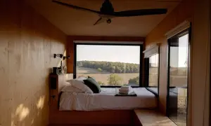 Intérieur d'une tiny house avec un lit douillet et une vue panoramique sur la campagne. Un endroit parfait pour se ressourcer.