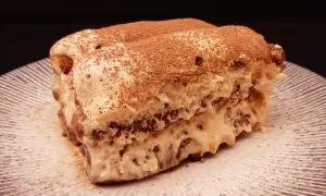 Une part de tiramisu au café, saupoudrée de cacao, sur une assiette striée. Un délice qui invite à découvrir la recette.