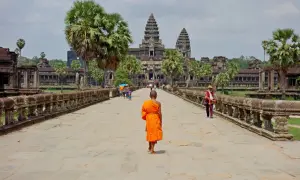 Mnich w pomarańczowej szacie idzie w stronę Angkor Wat, symbolu kambodżańskiej wycieczki.