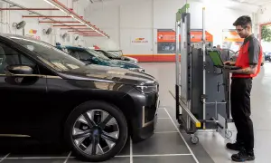 Técnico en taller revisa datos en laptop para calibrar máquina de corte de lunas de autos.