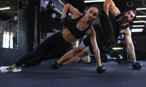 Para trenująca CrossFit wykonuje ćwiczenie z hantlami w pozycji bocznej deski.