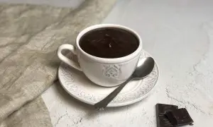 Una tazza di cioccolato caldo fumante, con cucchiaino e tavolette di cioccolato fondente accanto.