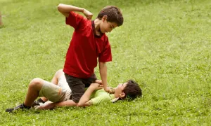 Un niño en camiseta roja agrede a otro en el suelo. Un ejemplo de cómo los niños que excluyen a otros pueden causar daño.