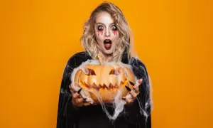 Przerażająca dziewczyna z makijażem na imprezę halloween trzyma wydrążoną dynię.