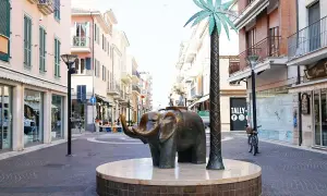 Scultura di elefante e palma sul centro passeggiata San Benedetto del Tronto, con negozi e palazzi colorati sullo sfondo.