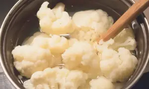 Gotowanie kalafiora w garnku. Drewniana łyżka miesza różyczki w gotującej się wodzie.