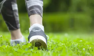Füße in Sportschuhen und Laufhose bewegen sich durch grünes Gras. Spazieren gehen ist Sport und gut für die Gesundheit.