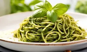 Spaghetti z zielonym pesto i listkami bazylii na białym talerzu.
