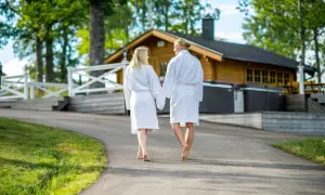 Ett par i badrockar går hand i hand mot en timrad stuga med utomhuspool. Kanske på väg till en avkopplande stund vid hvide sande.