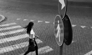 Una donna attraversa la strada su un selciato, seguendo le indicazioni di un segnale pedonale. Fotografia di strada.