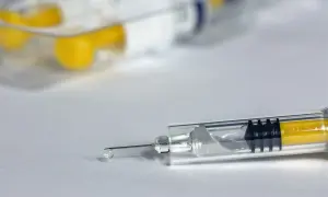 Zbliżenie na strzykawkę z żółtym płynem i kroplą na igle.