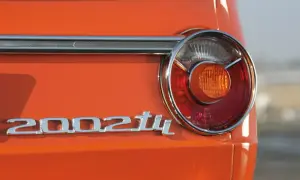 Detalle de la parte trasera de un BMW 2002 Tii naranja, con su icónico emblema cromado y una luz trasera circular.