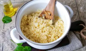 Frisch zubereiteter Couscous in einem Topf, bereit zum Servieren. Ein Holzlöffel lockert die Körner auf.