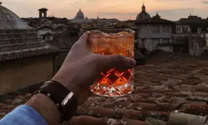 Un bicchiere di aperitivo con vista sui tetti di Roma centro al tramonto. Un momento perfetto per un apericena indimenticabile.