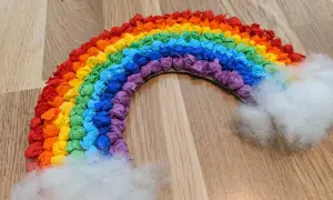 Ein farbenfroher Regenbogen, gebastelt aus zerknülltem Krepppapier, mit flauschigen Wolken an den Enden.