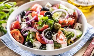 Ensalada griega fresca con tomates, pepinos, aceitunas negras y verdes, cebolla morada y queso feta, adornada con perejil.