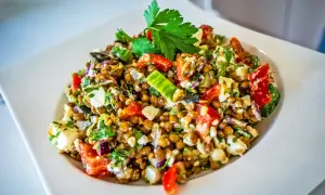 Ein bunter Linsensalat mit Feta, Tomaten, Gurken und frischer Petersilie, garniert mit einem Petersilienblatt.