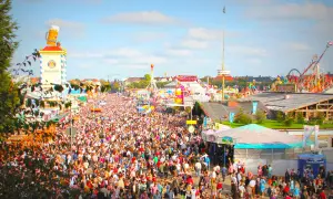 Folla immensa in **la città dell'Oktoberfest**, tra giostre, bancarelle e la torre Paulaner con un boccale di birra gigante.