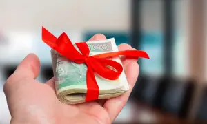 Dłoń trzyma zwinięte banknoty 100 zł przewiązane czerwoną wstążką. To prezent, kiedy nie trzeba zgłaszać darowizny do urzędu skarbowego.