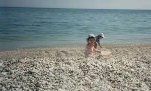 Bambini giocano sulla spiaggia di ciottoli a Marina di Montemarciano, con il mare azzurro sullo sfondo.