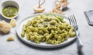 Fusilli z aromatycznym makaronem z pesto ze słoika, posypane parmezanem. Obok miseczka z sosem, kawałki sera i orzeszki piniowe.