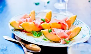 En vacker tallrik med melon och skinka, garnerad med basilika och peppar. Perfekt för en lätt och elegant förrätt.