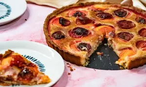 Une délicieuse tarte aux prunes rouges, garnie de poudre d'amande, est prête à être dégustée. Une part a déjà été servie.