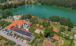 Widok z lotu ptaka na ośrodek wypoczynkowy nad turkusowym jeziorem. Widać budynki, domki, pole namiotowe, kampery i plażę. To idealne miejsce na wypoczynek, niczym złota łania wiartel.