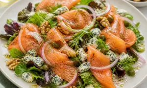 Salade colorée avec saumon fumé, fromage bleu émietté, noix, câpres et oignons rouges sur un lit de verdure.