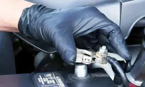 Ręka w czarnej rękawiczce dokręca śrubę na klemie akumulatora samochodowego.