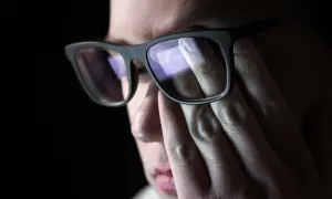 Mroczki przed oczami po wstaniu, gdy ręka z okularami zasłania twarz.