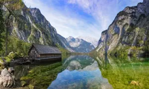 Holzhütte am Königssee, ein Juwel in Bayern, spiegelt sich im klaren Wasser vor majestätischen Bergen.