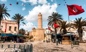 Placez-vous ici pour savoir où aller en Tunisie : une place animée avec des drapeaux tunisiens, des palmiers et une tour historique.