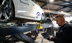 Mechaniker prüft mit Tablet die Achsvermessung an einem Auto. Die Spur verstellt, wird hier präzise eingestellt.