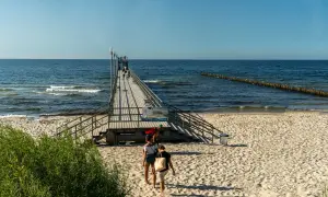 Spacerem po molo w słoneczny dzień. W tle morze i falochrony. Wiele atrakcji czeka na plaży.