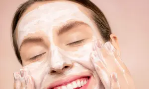 Donna sorridente con maschera bianca sul viso, mentre impara come fare una pulizia del viso a casa.