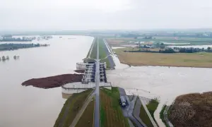 Ogromna tama i budowle hydrotechniczne walczą z żywiołem. Woda sięga pól uprawnych, a w oddali widać zalane tereny. To obraz powodzi błyskawicznej.