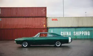 Klasyczny zielony **hatchback** Dodge Charger z białym pasem na tyle, zaparkowany przy stosach kontenerów w porcie.