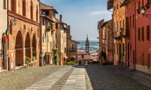 Rue pavée bordée de maisons colorées, avec une église au loin. Un charmant village du Piémont, Italie.