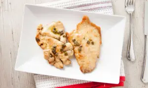 Due fette di fesa di tacchino con capperi su un piatto bianco. Un pasto leggero, ideale per chi cerca fesa di tacchino calorie.