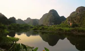 Krajobraz Ninh Binh z odbijającymi się w wodzie wapiennymi górami porośniętymi zielenią.
