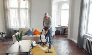 Mężczyzna odkurza dywan w salonie. Sprzątanie w domu to jego sposób na relaks.